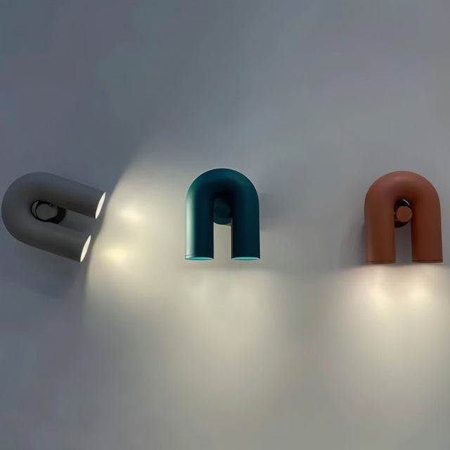 "Three contemporary wall lamps, in gray, blue, and red, mounted on a gray wall, showcasing their looped design and adjustable light direction."