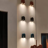 "Multiple contemporary wall lamps in red, black, and blue, arranged in a vertical row on a white wall, showcasing a unique, looped design and adjustable lighting."