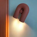 "A close-up of a red, contemporary wall lamp with a looped design, showing the light emitted from its adjustable dual sources."