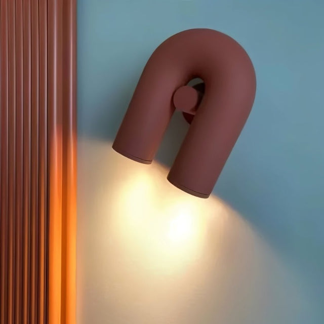 "A close-up of a red, contemporary wall lamp with a looped design, showing the light emitted from its adjustable dual sources."