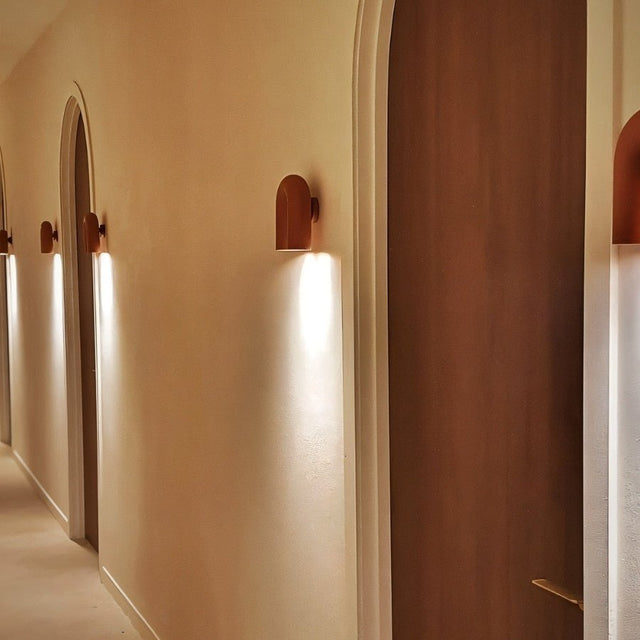 "Several red, contemporary wall lamps with a looped design, illuminating a hallway with arched doorways."