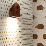 "A red, contemporary wall lamp with a looped design, mounted on a patterned wallpaper in a child's room."