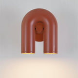 "A front view of a red, contemporary wall lamp with a looped design, showing its dual light sources illuminated against a white background."