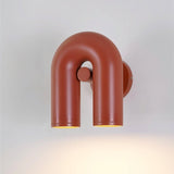 "A red, contemporary wall lamp with a distinctive looped design, featuring two illuminated light sources against a light background."
