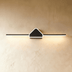 Black modern vanity light fixture above illuminated rectangular mirror with wooden cabinet in tile bathroom.