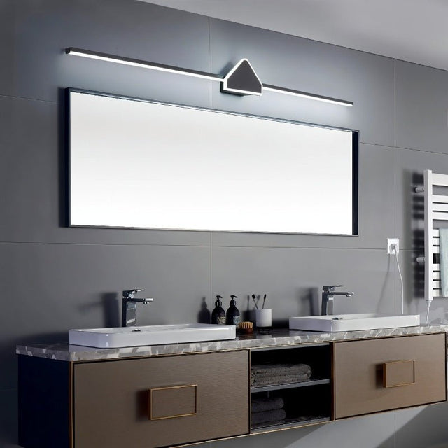 "A modern black wall lamp with a geometric centerpiece and streamlined bar, mounted above a large rectangular mirror in a contemporary bathroom with dual sinks."