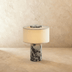 Modern cylindrical table lamp with white shade and decorative textured base on white background, front view.