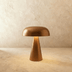 Cream upholstered bed with white pillows and rumpled linens beside black mushroom-shaped table lamp on dark side table, lifes