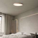 "A modern travertine flush mount ceiling light with a circular design, providing soft ambient lighting in a minimalist bedroom with a large window and white bedding."