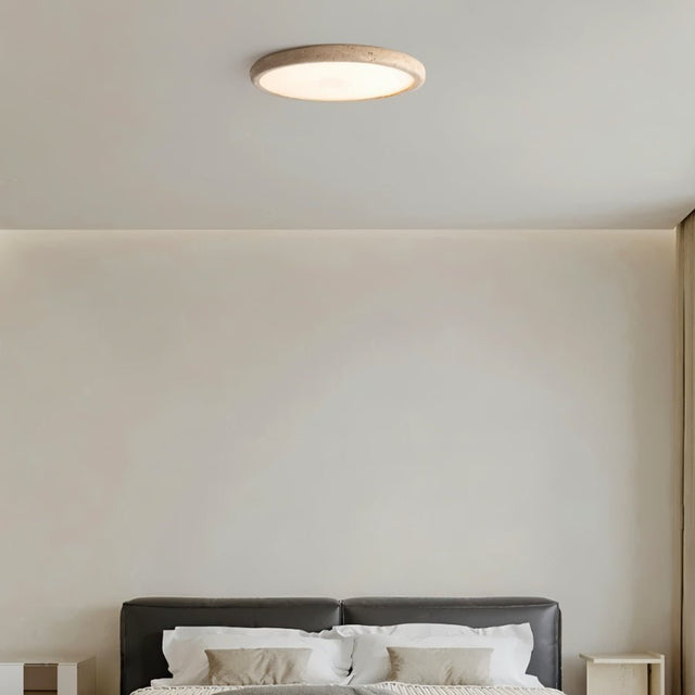 "A modern travertine flush mount ceiling light with a circular design, providing ambient lighting in a minimalist bedroom."