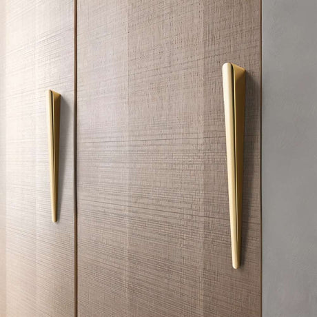 "Two sleek, tapered zinc alloy pull bars with a geometric profile in a gold finish on a modern wooden cabinet."