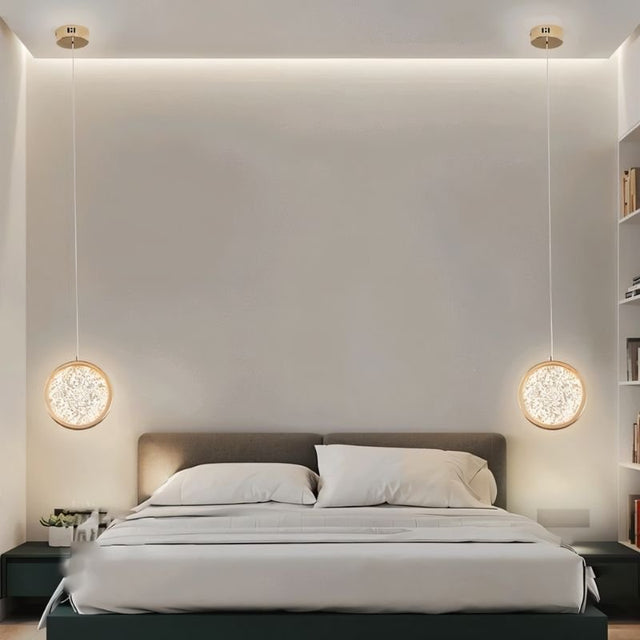 "Two gold ring pendant lights with crystal-like centers, hanging on either side of a bed in a room with white walls."