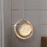"A gold ring pendant light with a crystal-like center, hanging in a room with a gray paneled wall."