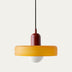 Pendant light with burgundy metal cap, yellow-gold shade, and white diffuser, hanging against neutral background.