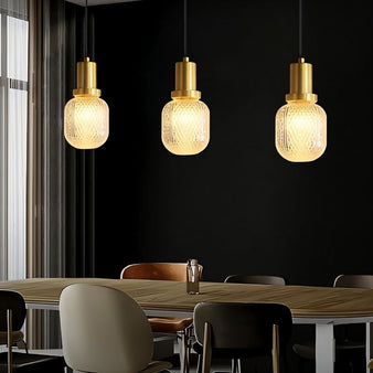 "Modern pendant lights with brass bases and patterned glass shades hanging over a contemporary dining table, creating a warm and inviting ambiance."