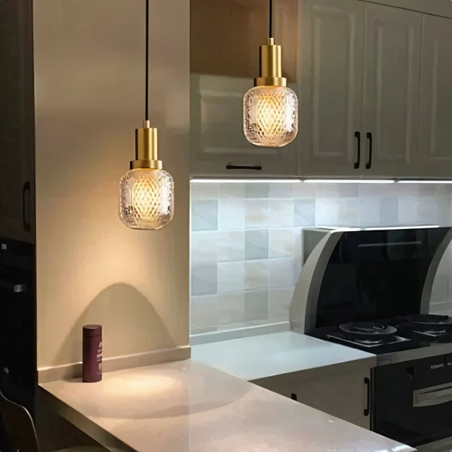 "Pair of modern pendant lights with brass bases and patterned glass shades, illuminating a contemporary kitchen island with a warm and inviting ambiance."