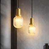 "Pair of modern pendant lights with cylindrical brass bases and patterned, crystal-clear glass shades, diffusing light for a warm, inviting ambiance."