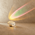 Clear glass dome paperweight on wooden base with colorful light projection on dark studio background