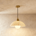Three cream pendant lights with brass hardware suspended against cork textured wall in modern interior setting.
