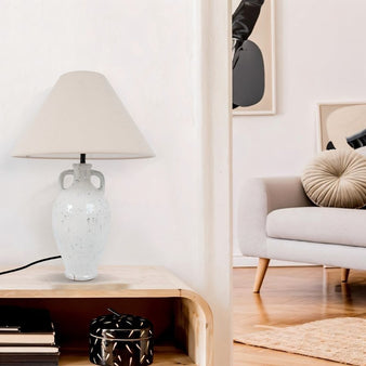 "A minimalist ceramic table lamp with a textured white base and a fabric shade, illuminating a modern living room."