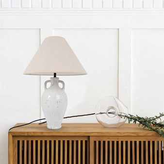 "A contemporary white ceramic table lamp with a classic lampshade, complementing a minimalist interior design."