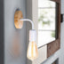 Wood and white metal wall sconce with vintage Edison bulb hanging near a sunlit window.