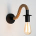 Wall lamp with black metal fixture and twisted rope arm holding a glowing Edison-style bulb against white background.