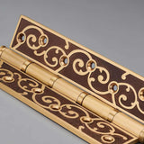 "Close-up of a brass door hinge with ornate scrollwork design and a polished finish."