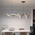 Modern wavy LED pendant light in black finish suspended above a white dining table in a contemporary kitchen.