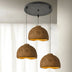 Three dome-shaped pendant lights with gold interior and textured brown exterior hang from a black ceiling fixture against a white wall.
