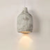Concrete pendant light with textured gray finish casting warm light downward on white wall.