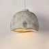 Concrete dome pendant light with warm gold interior illuminated against neutral background.