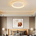 Oval LED ceiling light with warm gold finish mounted above a modern bedroom with tan upholstered headboard.