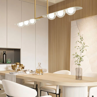 "Copper Dilti pendant light with glass globes hanging above a light wood dining table with white chairs."