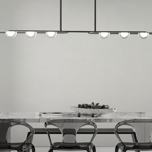 "Copper Dilti pendant light with glass globes hanging above a dining table with transparent chairs."