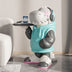 White dinosaur figurine wearing turquoise jacket and headphones, holding tray with cup, seated on wooden floor next to white couch.