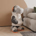 Cream and black dinosaur figurine wearing headphones and boxing gloves, seated indoors beside a beige sofa.