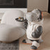 Playful white and black dinosaur floor figurine with orange accents holding a small table in a modern living room setting.