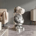 Stylized dinosaur figurine with silver metallic finish and headphones, displayed on polished concrete floor in modern living room.