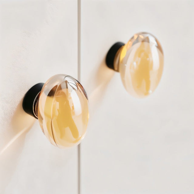 "Two amber crystal glass spherical knobs with ribbed texture on a white cabinet."