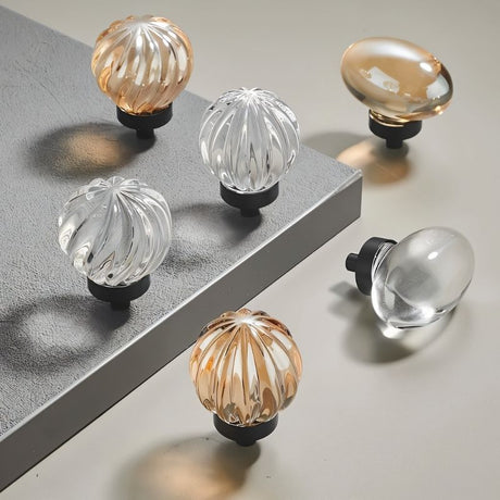 "Set of crystal glass knobs in spherical and oval shapes with ribbed and smooth textures."