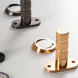 "Close-up of modern magnetic door stops with textured cylindrical posts and oval mounting plates in brushed nickel and gold finishes."