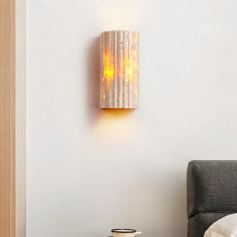 "A minimalist, rectangular travertine wall lamp mounted on a bedroom wall, providing a soft, warm glow above a bed."