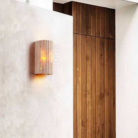 "A minimalist, rectangular travertine wall lamp mounted on a textured wall in a modern hallway with wooden paneling, providing a soft, ambient glow."