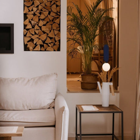 "This contemporary Dorea Pendant Lamp, featuring a glass bulb and metal frame, complements a stylish dining area with a vertical fabric panel and soft lighting."