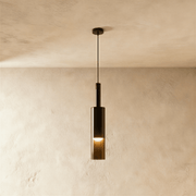 Black cylindrical pendant light with gold accent, hanging above green upholstered bed in modern bedroom setting.