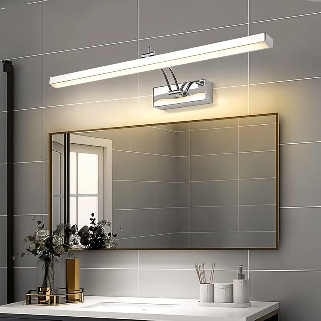 "A modern, minimalist LED wall lamp with a polished stainless steel body, mounted above a bathroom mirror with a dark frame."