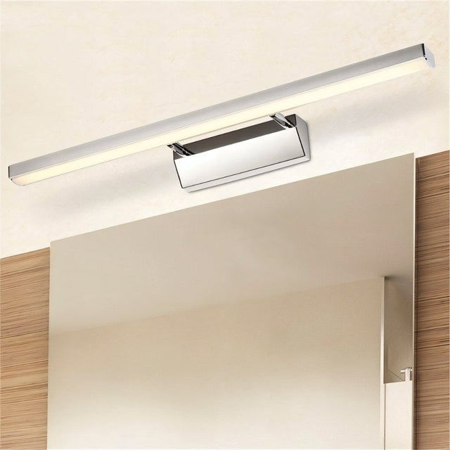 "A modern, minimalist LED wall lamp with a polished stainless steel body, mounted horizontally above a light-colored bathroom vanity mirror."