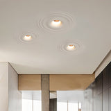 "Three white ceiling lights with concentric circles, installed flush in a white ceiling of a modern hallway with paneled walls."