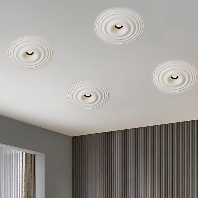 "Four white ceiling lights with concentric circles, installed flush in a white ceiling of a modern room with gray walls and a window."
